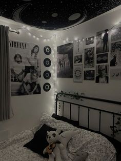 a bedroom decorated in black and white with pictures on the wall, lights strung from the ceiling