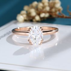 a rose gold engagement ring with a round brilliant diamond in the center, sitting on top of a white card