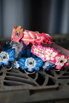 three colorful bracelets sitting on top of a metal grill grate with flowers painted on them