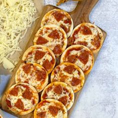 small pizzas are on a cutting board next to cheese and other foodstuffs