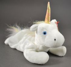 a white stuffed unicorn laying down with a gold horn on its head and tail,