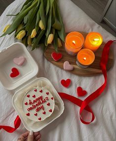 someone is holding a cake in front of some candles and tulips on a bed