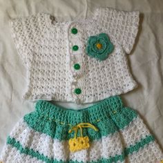 two crocheted baby clothes are laying on a white sheet with yellow and green trims