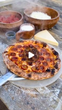 a pizza sitting on top of a wooden table next to bowls and utensils