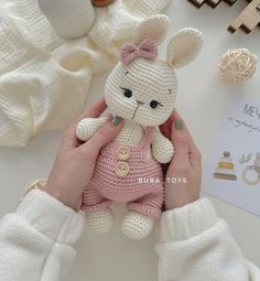 a crocheted bunny doll is held by someone's hands on a table