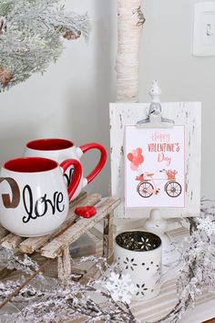 two coffee mugs sitting on top of a table next to a sign that says i love valentine's day