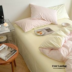 a bed with pink sheets and pillows on top of it next to a small table