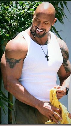 a bald man in white shirt holding a banana and smiling at someone with tattoos on his arm