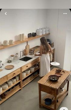 a woman standing in a kitchen next to a table with bowls and plates on it