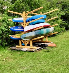 a bunch of surfboards stacked on top of each other in the grass next to trees