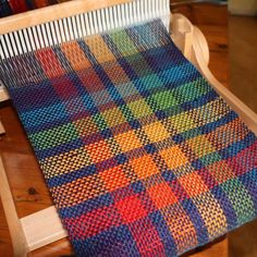 a multicolored knitted blanket sitting on top of a wooden chair next to a pile of yarn