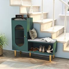 there is a green cabinet with shoes on it in front of the stairs and potted plant