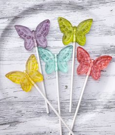 four butterfly lollipops sitting on top of a white wooden table next to a plate