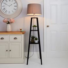 a clock on the wall next to a shelf with flowers and potted plants in it