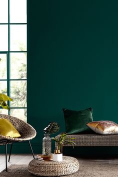 a living room with green walls and wicker furniture in the corner, along with plants