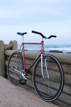 a red bike leaning against a wooden fence near the ocean with waves in the background