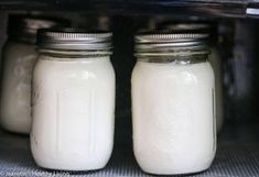 two jars filled with white liquid sitting on top of an oven door sill next to each other