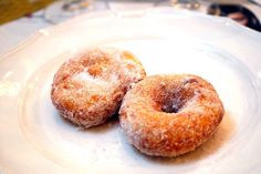 two sugared donuts sitting on top of a white plate