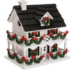 a white birdhouse decorated with red bows and wreaths