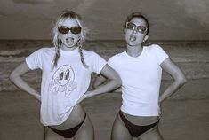 two women in bathing suits standing on the beach with their hands on their hipss