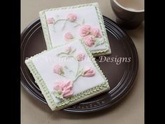 two square decorated cookies sitting on top of a plate next to a cup and saucer