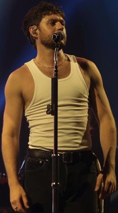 a man standing in front of a microphone with his hands on his hips and wearing black pants