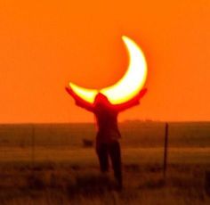 a person standing in a field with their arms spread out to the side, as the sun sets behind them