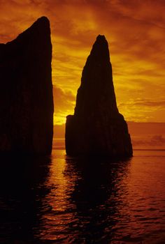 two large rocks sticking out of the water at sunset