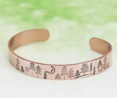 a copper bracelet with trees and the moon on it, sitting against a green background