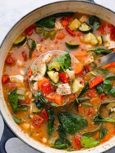 a ladle full of vegetable soup being spooned into the pot with vegetables in it