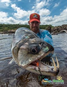 a man holding a large fish with its mouth open and teeth out in the water