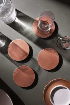 four copper coasters on a table with cups and saucers next to each other