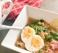 a white bowl filled with soup and topped with hard boiled eggs on top of spinach