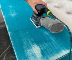 a person sanding down a blue surfboard with an electric sander