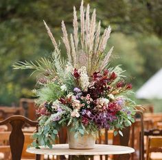 an arrangement of flowers and greenery in a vase on top of a small table