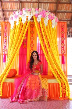 a woman sitting in front of an orange and yellow stage with flowers on the wall