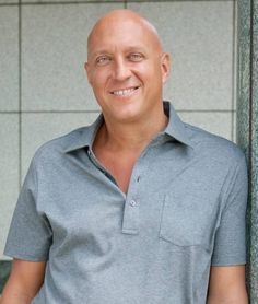 a bald man wearing a gray shirt standing in front of a building