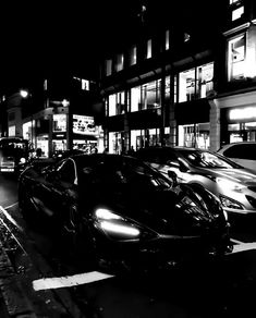 black and white photograph of cars parked on the side of a street in front of tall buildings at night