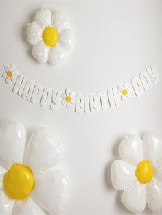 white and yellow flowers are placed on the table with happy birthday banner in the background