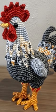 a crocheted chicken standing on top of a wooden table next to a white wall