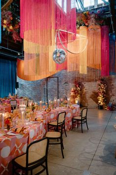 the tables are set for an event with orange and pink decorations hanging from the ceiling