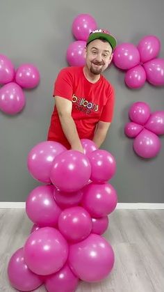 a man standing on top of a pile of pink balloons in front of a gray wall