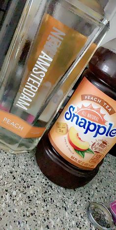 a bottle of apple cider next to an empty glass container on a counter top