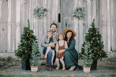 a man, woman and child are sitting in front of christmas trees with their arms around each other