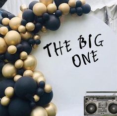 there is a sign that says the big one with balloons on it and a boombox next to it