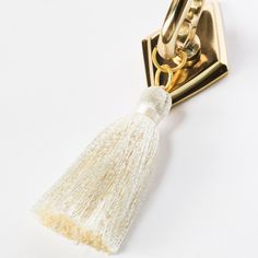 a white and gold tasseled keychain on a white surface