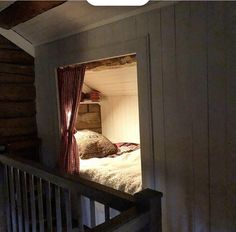 an open door leading to a bed in a room with wooden walls and flooring