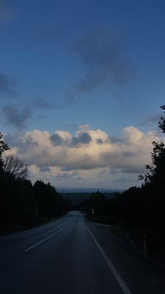 an empty road with trees and clouds in the background