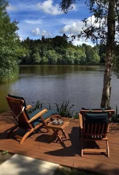 two lawn chairs sitting on top of a wooden deck next to a tree and water