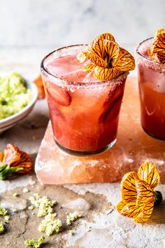 two cocktails with orange flowers on the rim and garnishes in the middle